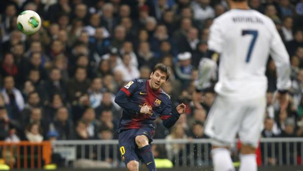 Lionel Messi schießt einen Fußball, während Cristiano Ronaldo zusieht.