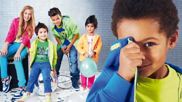 Eine Gruppe Kinder in bunter Kleidung feiert mit Luftballons und einer Discokugel.