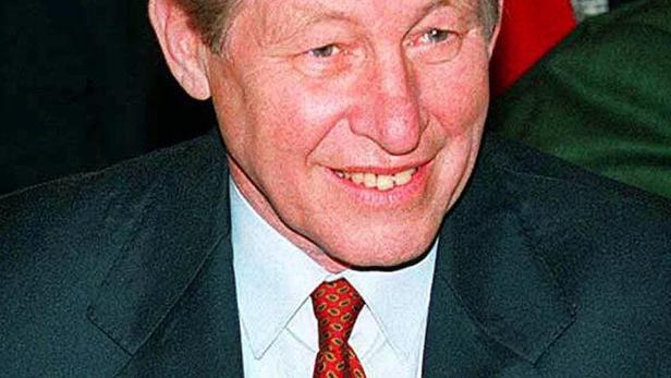 Ein lächelnder Mann mit Anzug und roter Krawatte.