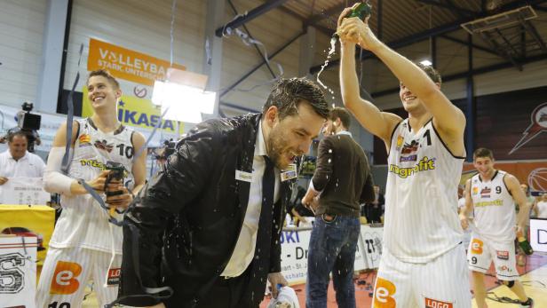 Ein Basketballtrainer wird von seinen Spielern mit Champagner übergossen, während diese ihren Sieg feiern.