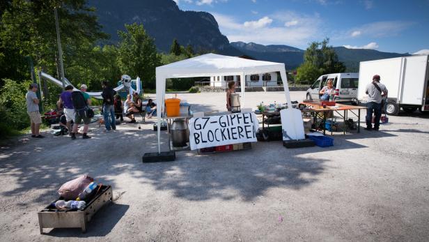 Eine Gruppe von Menschen demonstriert unter einem Zelt gegen den G7-Gipfel.
