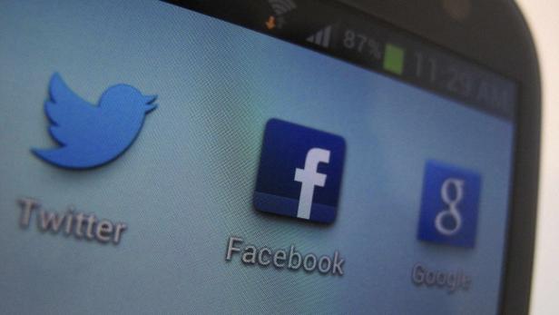 Auf dem Bildschirm eines Smartphones sind die Logos von Twitter, Facebook und Google zu sehen.
