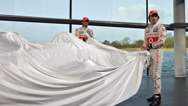 Zwei Rennfahrer enthüllen ein neues Formel-1-Auto unter einem weißen Tuch.