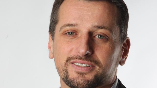 Porträt eines Mannes mit Bart und grünen Augen vor einem weißen Hintergrund.