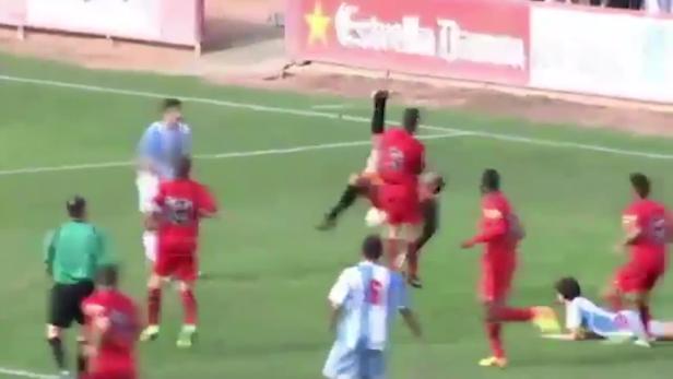 Während eines Fußballspiels springt ein Spieler in Rot über einen am Boden liegenden Spieler.