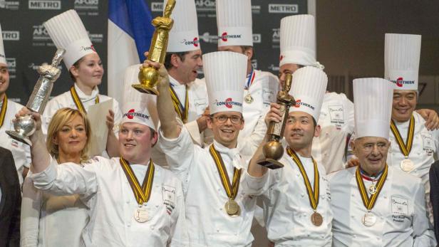 Eine Gruppe von Köchen in Kochuniformen und mit Medaillen posiert mit Trophäen.