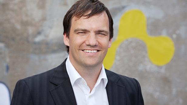 Ein lächelnder Mann im Anzug vor einer Wand mit Graffiti.