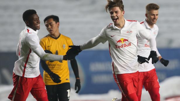 Ein jubelnder Fußballspieler im Trikot von Red Bull wird von seinen Teamkollegen beglückwünscht.