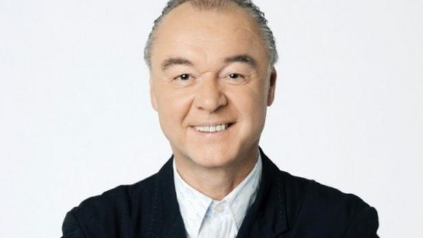 Ein lächelnder Mann in einem dunklen Sakko vor einem weißen Hintergrund.