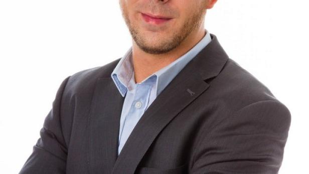 Ein Mann im Anzug mit verschränkten Armen vor einem weißen Hintergrund.