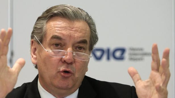 Ein Mann mit Brille gestikuliert vor einem Logo.
