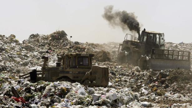 Zwei Bulldozer schieben Müll auf einer riesigen Mülldeponie zusammen, wobei einer Rauch ausstößt.