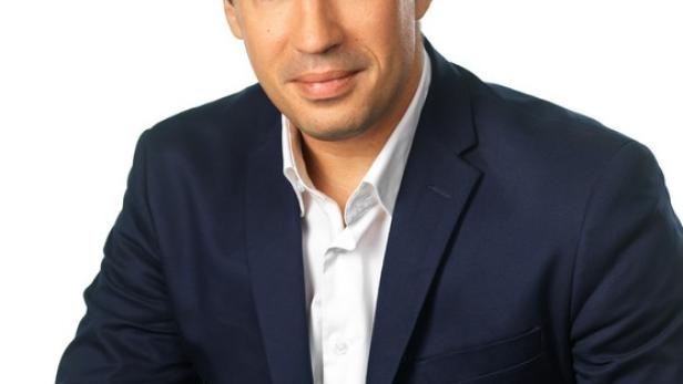 Ein Mann in einem blauen Anzug sitzt vor einem weißen Hintergrund.