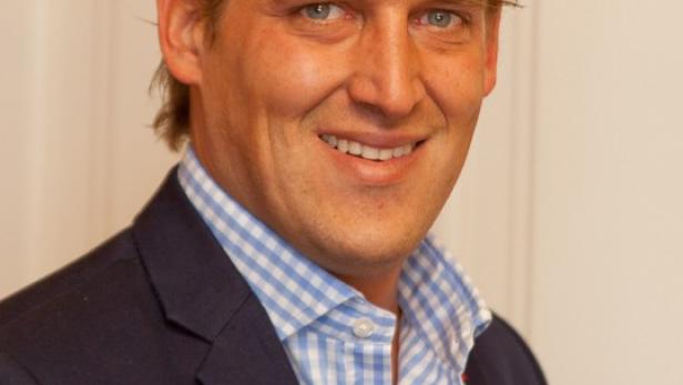 Ein Mann mit blonden Haaren und blauem Hemd lächelt in die Kamera.