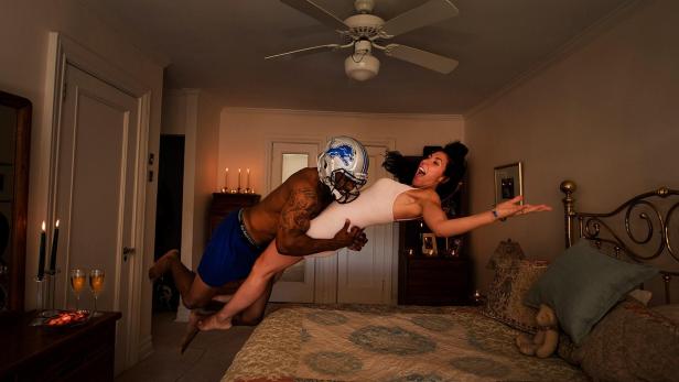 Ein Mann mit Footballhelm trägt eine Frau im Schlafzimmer.