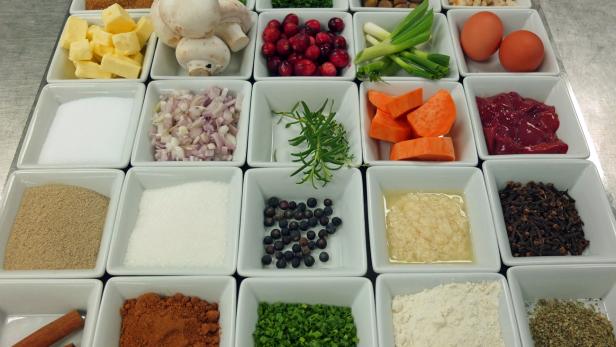 Verschiedene Zutaten wie Gemüse, Gewürze und Kräuter in kleinen weißen Schalen angerichtet.