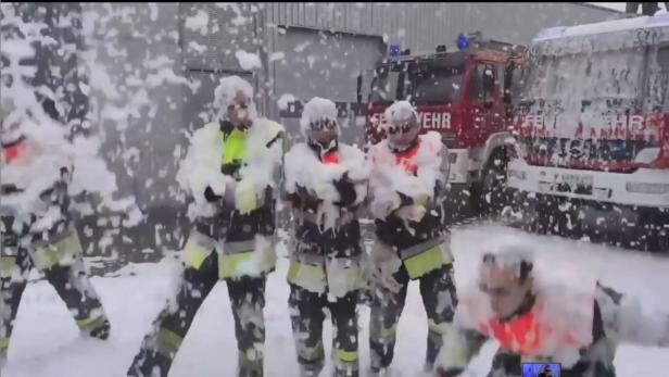 Feuerwehrleute stehen vor ihren Feuerwehrwagen und sind mit Schaum bedeckt.