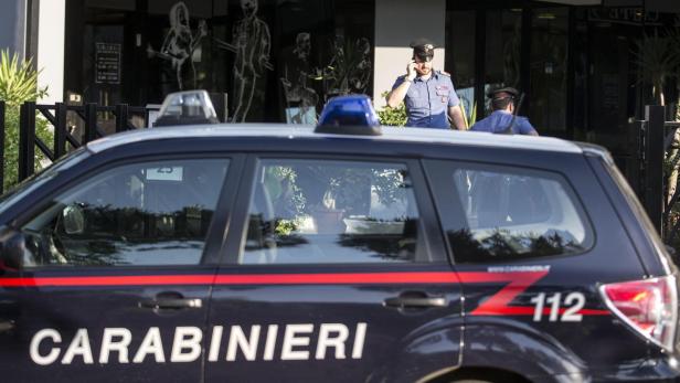 Ein Carabinieri-Fahrzeug steht vor einem Gebäude, während ein Polizist telefoniert.