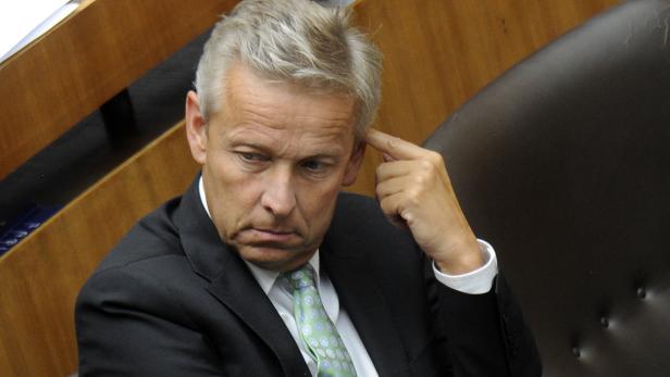 Ein Mann im Anzug sitzt nachdenklich da und berührt seine Stirn.