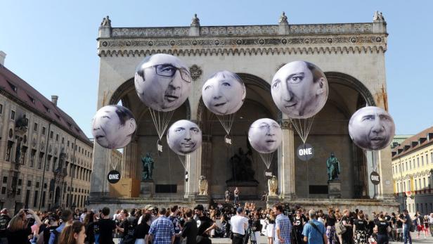Ballons mit den Gesichtern von Politikern schweben über einer Menschenmenge in München.