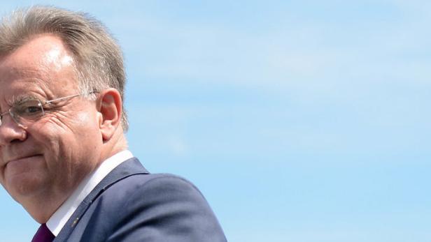 Ein Mann mit Brille und Anzug vor blauem Himmel.