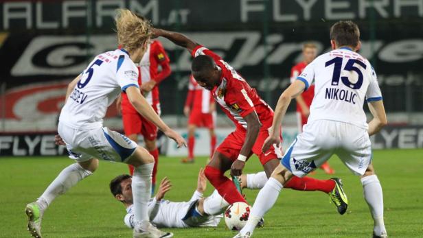 Ein Fußballspieler in Rot dribbelt den Ball, umgeben von Gegenspielern in weißen Trikots.