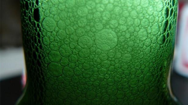 Nahaufnahme der Oberfläche einer grünen Glasflasche mit vielen kleinen Bläschen.