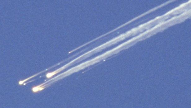 Mehrere Trümmerteile fallen mit Rauchfahnen vom Himmel.
