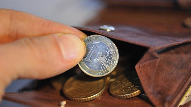 Eine Hand nimmt eine 1-Euro-Münze aus einem braunen Ledergeldbeutel.