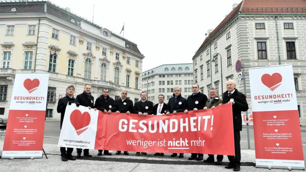 Eine Gruppe von Männern hält ein rotes Banner mit der Aufschrift „Gesundheit! Weniger ist nicht mehr“.