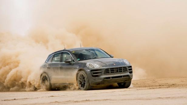 Ein grauer Porsche Macan fährt durch eine Staubwolke im Gelände.