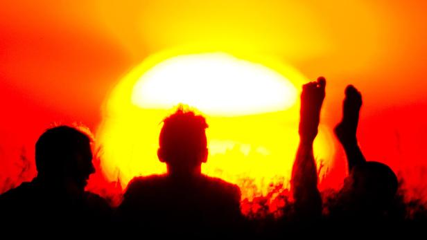 Silhouetten von drei Personen vor einem hellen, orangefarbenen Himmel.