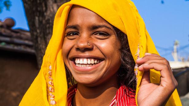 Eine lächelnde junge Frau mit gelbem Kopftuch und Nasenpiercing.