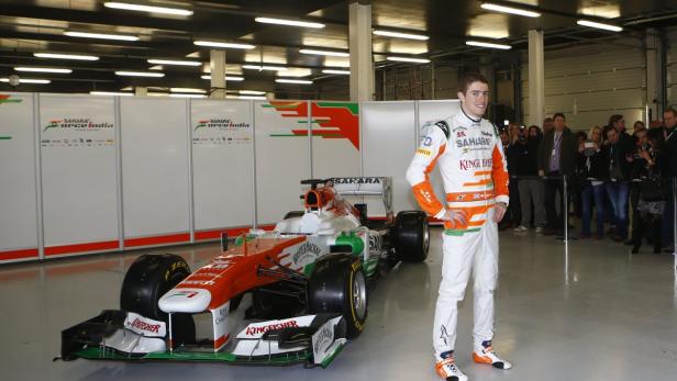 Ein Rennfahrer posiert neben einem Formel-1-Wagen des Teams Sahara Force India.