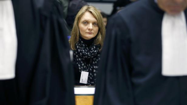 Eine Frau steht inmitten von Personen in Roben vor Gericht.