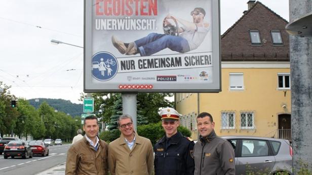 Eine Gruppe von Personen steht vor einer Verkehrssicherheitskampagne mit dem Slogan „Egoisten unerwünscht. Nur gemeinsam sicher!“.