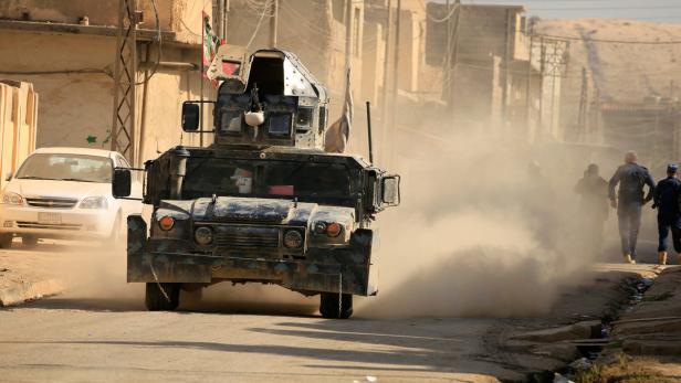 Ein gepanzertes Militärfahrzeug fährt eine staubige Straße entlang.