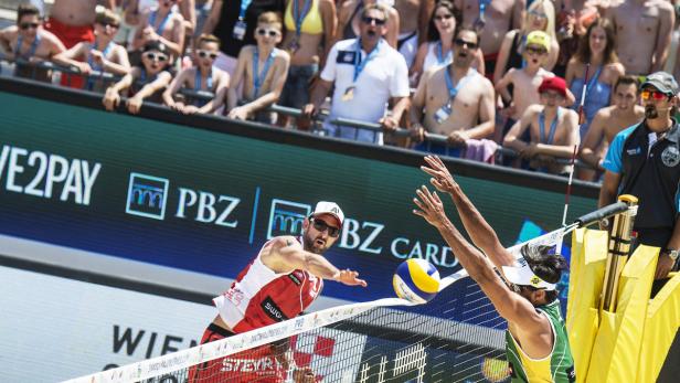 Zwei Beachvolleyballspieler kämpfen am Netz um den Ball, im Hintergrund Zuschauer.