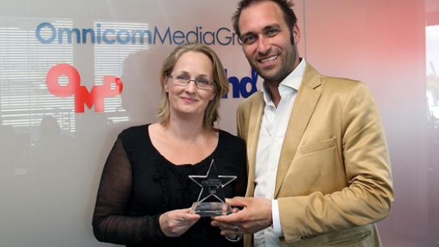 Zwei Personen halten eine Auszeichnung vor dem Logo von Omnicom Media Group.