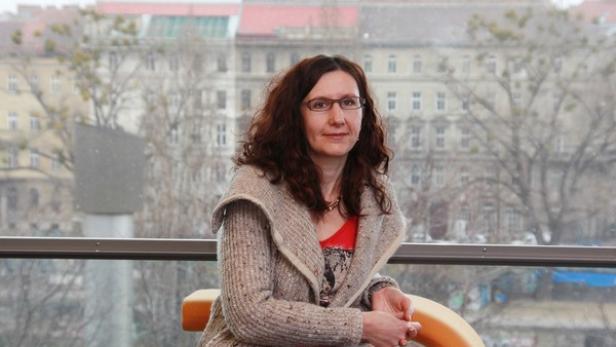 Eine Frau mit Brille sitzt vor einem Fenster mit Blick auf eine Stadt.