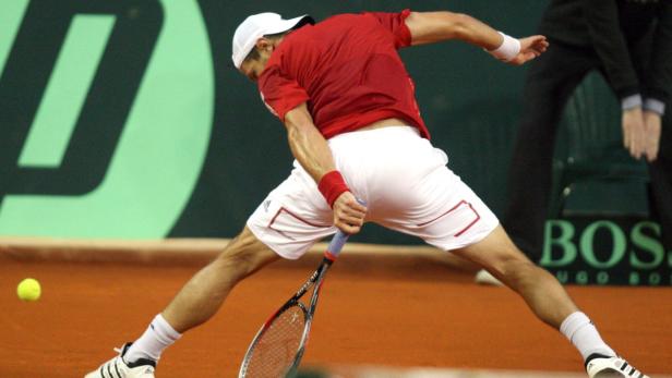 Ein Tennisspieler schlägt einen Ball auf einem Sandplatz.