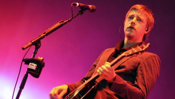 Ein Mann mit Gitarre singt auf einer Bühne mit rotem Licht.