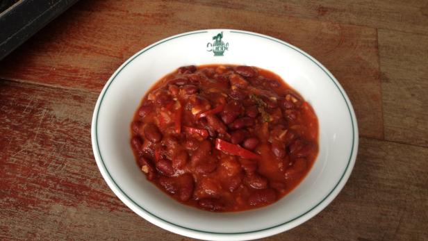 Ein Teller mit Chili con Carne steht auf einem Holztisch.