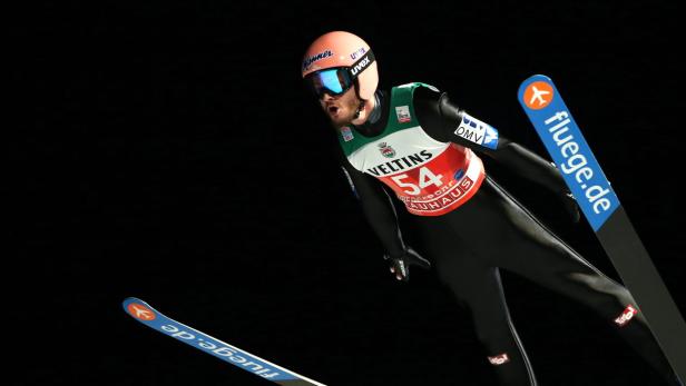 Ein Skispringer in der Luft vor einem schwarzen Hintergrund.