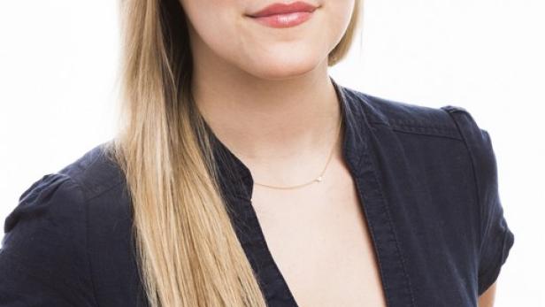 Eine Frau mit blonden Haaren und einem dunklen Hemd lächelt in die Kamera.