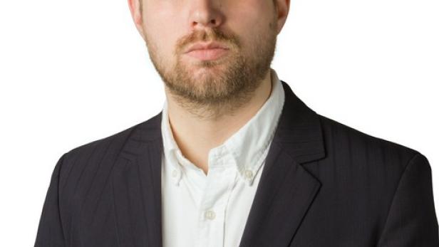 Ein Mann mit Bart und Anzug vor einem weißen Hintergrund.
