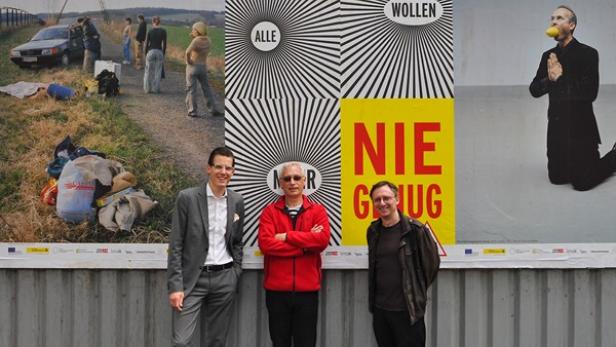 Drei Männer stehen vor einer Wand mit Kunstplakaten.