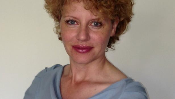 Porträt einer Frau mit lockigem, rötlichem Haar und einem hellblauen Oberteil.