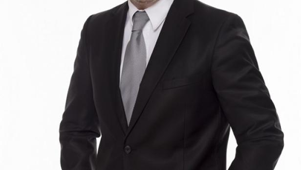 Ein lächelnder Mann im Anzug mit Krawatte und einer Armbanduhr.