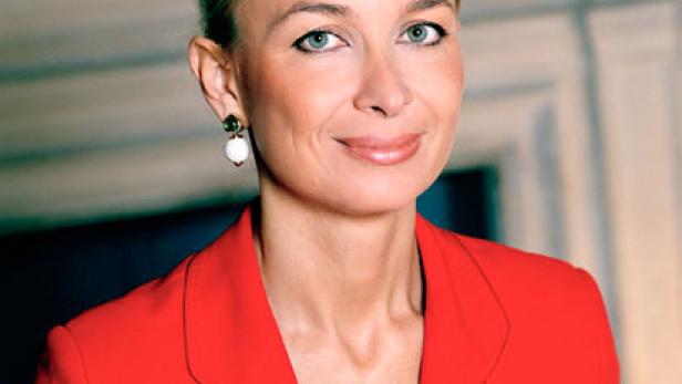 Eine Frau mit blonden Haaren und einem roten Blazer lächelt in die Kamera.